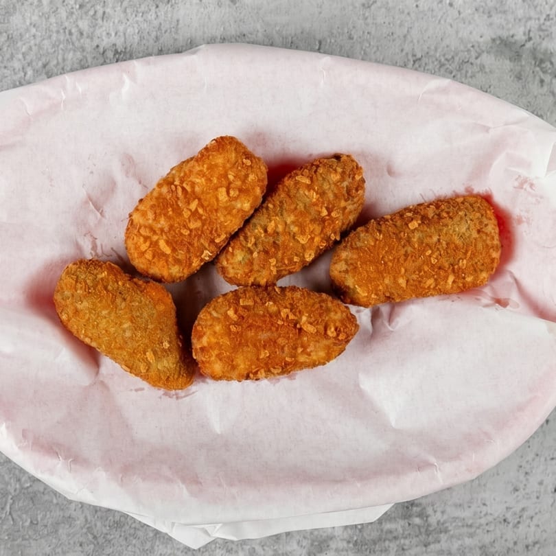 Five golden-brown fried jalapeño poppers with crispy breading, served on white paper in a basket.