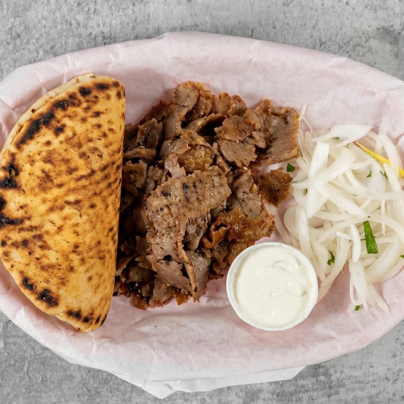 Gyro meat platter with pita bread, sliced onions, and a side of tzatziki sauce.