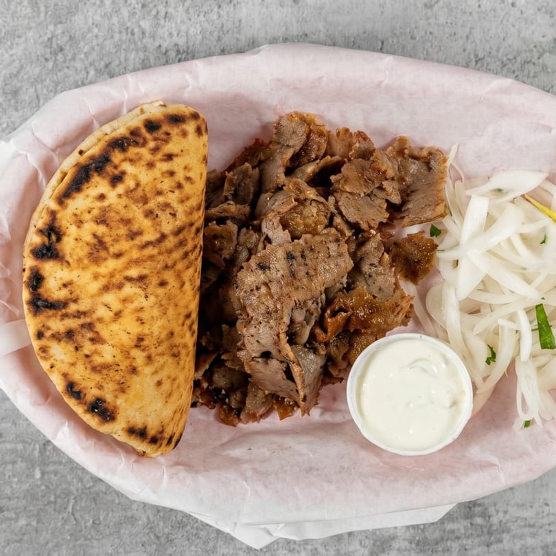 Gyro platter with sliced meat, pita bread, white onions, and a side of tzatziki sauce.